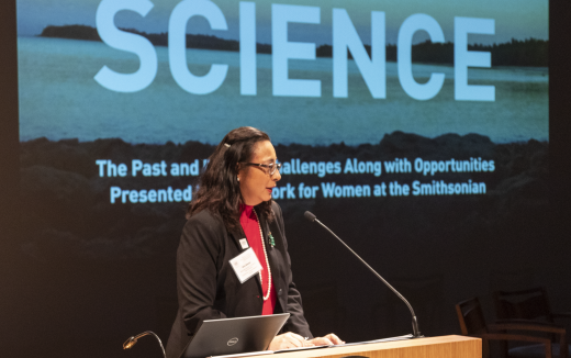 Oris Sanjur speaks at a podium. The words "Women in Science" are projected on a screen behind her.